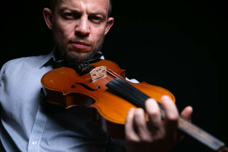 A man in a blue shirt plays the violin on a black background.の写真素材