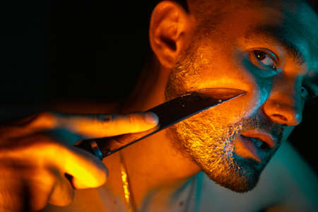 a man shaves with a knife in a neon light.の写真素材