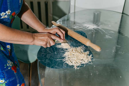 An unrecognizable woman cuts noodles. women's hands close-up.の写真素材