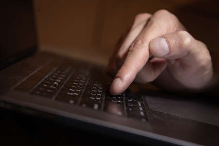 a man's hand presses the keyboard of a laptop with his finger.
