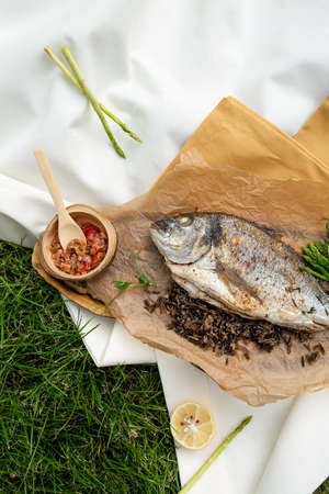 Grilled Dorado fish on a wooden board with paper with lemon, salad, sauce. top view.の写真素材