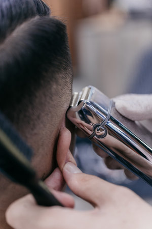 barber cutting hair using an electric hair clipper in a barber shop, focus on the electric hair...
