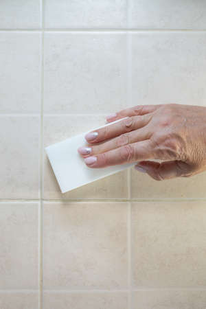 hand with a white melamine sponge washes the tile.