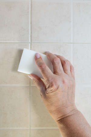 hand with a white melamine sponge washes the tile.