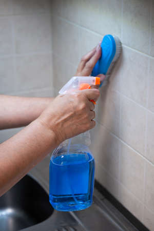 A man's hand cleans a tile wall with a blue brush.