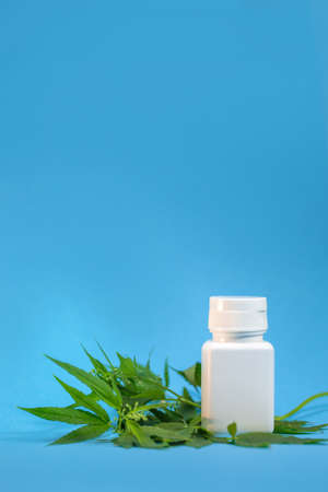 a white jar of medicines with a branch of cannabis on a blue background.の写真素材