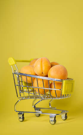 apricots in a small shopping cart on a yellow background.の写真素材