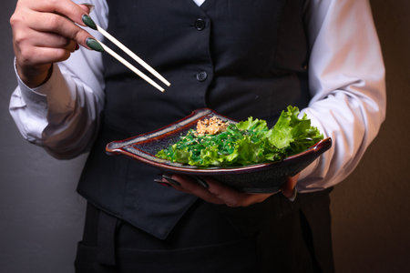 a girl without a face holds in her hands a plate of Japanese salad with chuka, lettuce leaves and sauce close-up.の写真素材