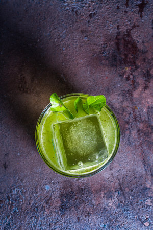 top view of a green cocktail in a glass with ice and a mint leaf on a textured background.の写真素材