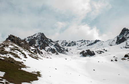 A winter landscape of snow-covered mountains and hills with a rocky summit in the distance and snow-covered hills in the foreground, taken on a bright day with a blue sky and white clouds.の写真素材
