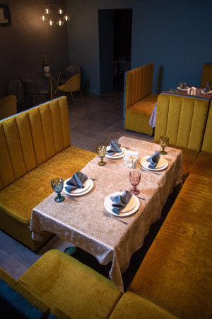 This image showcases an elegant restaurant interior with a table set for four, yellow booths, and ambient lighting, ideal for fine dining or a romantic dinner for two.の写真素材