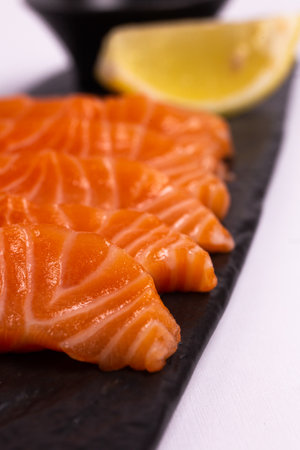 A close-up of a fresh salmon fillet garnished with lemon wedges and soy sauce on a black stone plate. This appetizing seafood dish is isolated on a white background, perfect for a healthy meal.の写真素材