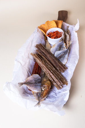The smoked fish includes salmon, trout, and whitefish. The fish is served on a wooden board with a bowl of red pepper flakes.の写真素材