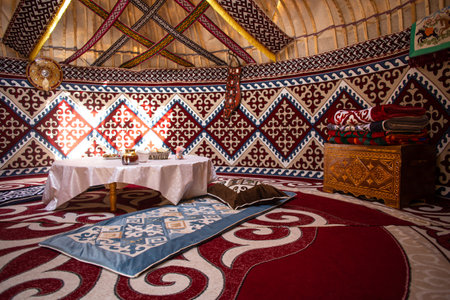 Interior of a kazak yurt with felt carpets, furniture, and a table. Traditional nomadic dwelling with white tablecloth.の写真素材