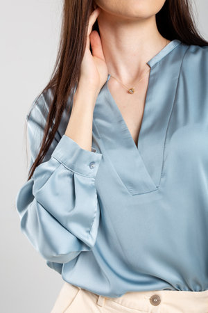 Young woman in blue satin blouse with plunging neckline, long sleeves, and smile. Brown hair, elegant look.の写真素材