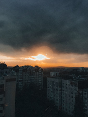 A stunning city skyline at sunset with a dramatic sky filled with dark clouds and the warm glow of...