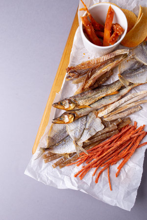 Assorted dried fish, fish skin, and fruit snacks on white paper on a wooden table, creating a vibrant culinary display.の写真素材