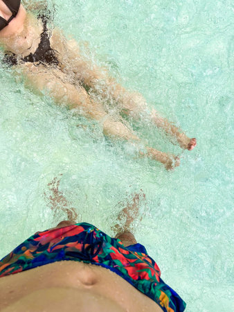 a guy and a girl with no faces in the pool. a guy in shorts and a girl in a swimsuit in a blue poolの写真素材