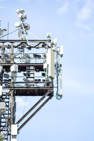 Cell tower with multiple antennas and satellite dishes against blue sky - modern communication...