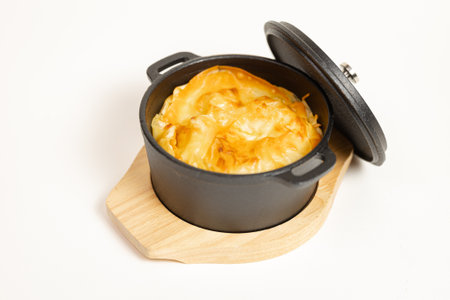 Golden baked casserole in cast iron pot on wooden stand. White background - perfect for menus, food...