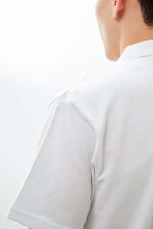 Rear view of a man wearing a white polo shirt against a light background. Minimalist shot highlighting fabric and shape, perfect for apparel mockups and fashion catalogs.の写真素材