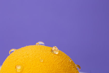 Close-up of a lemon-shaped dessert: extreme macro shot highlighting the granular yellow surface and glistening water droplets.の写真素材