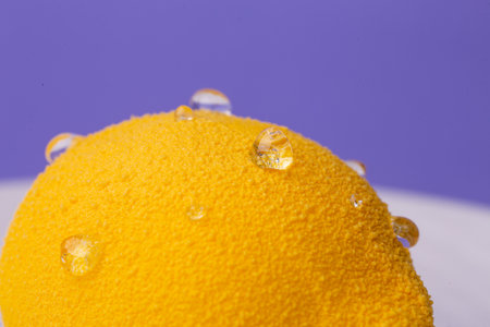 Close-up of a lemon-shaped dessert: extreme macro shot highlighting the granular yellow surface and glistening water droplets.の写真素材