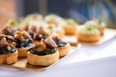 Appetizing tarts with stewed mushrooms and spinach in close-up on a golden tray, served outdoors. Canape with mushrooms and spinach - appetizing mini tartlets on gold trayの写真素材