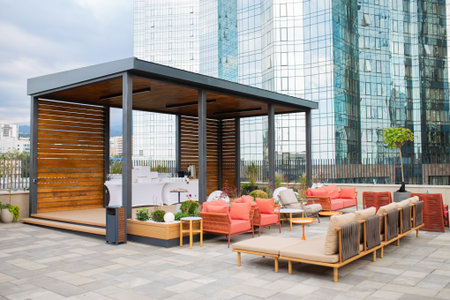 Modern rooftop lounge with seating area, wooden pavilion, and panoramic backdrop of glass skyscrapers. Perfect for hotel, coworking, or luxury real estate adsの写真素材