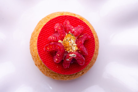 Overhead shot of a dessert: crisp base, red layer, perfectly arranged raspberries, and edible gold...