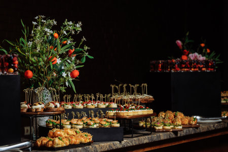 Elegant buffet table featuring mini sandwiches, pastries, canapes and fresh blooms against a moody...