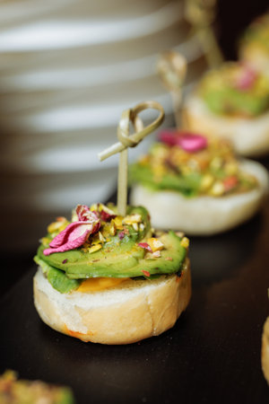 Mini toasts topped with creamy avocado, crushed nuts and delicate petals - ideal for luxury catering or gourmet food branding.の写真素材