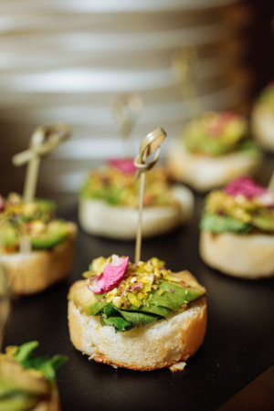 Mini toasts topped with creamy avocado, crushed nuts and delicate petals - ideal for luxury catering or gourmet food branding.の写真素材