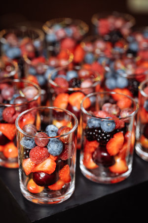 Individual servings of vibrant strawberries, blueberries, blackberries and cherries in transparent...