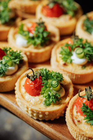 Close-up of mini tartlets with cherry tomatoes, cucumber, and fresh herbs on a wooden board. Light background, natural lighting, appetizing presentation.の写真素材