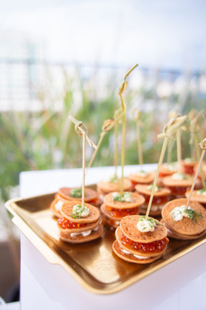 Delicate bite-sized pancakes topped with cream cheese and vibrant caviar - perfect for luxury catering or upscale event visuals.の写真素材