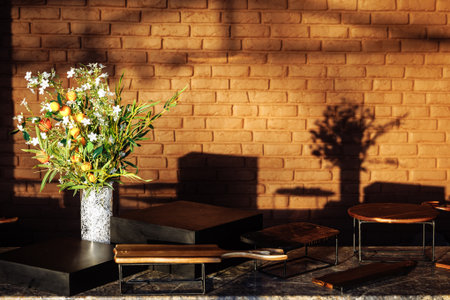a decorative floral arrangement with white flowers and small fruits placed in a vase near a brick wall illuminated by warm direct sunlightの写真素材