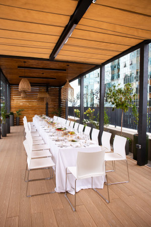 Wide shot of long set table on terrace with city view - elegant table setting for event