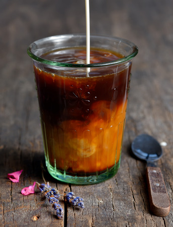 Pouring milk into a glass of black coffee. Isolated on blackの写真素材