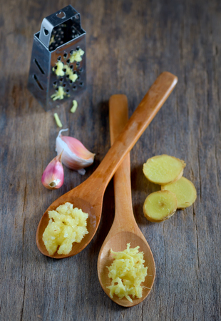 garlic and ginger in wooden spoons on wooden tableの写真素材