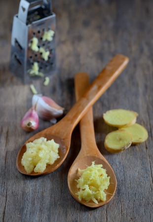 garlic and ginger in wooden spoons on wooden tableの写真素材