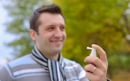 Young man using throat spray in cold seasonの写真素材