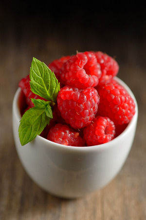 ripe and fresh raspberry in white cup on wooden tableの写真素材