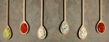 different types of sauces in spoons on stone tableの写真素材