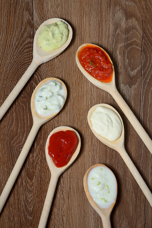 different types of sauces in spoons on wooden tableの写真素材