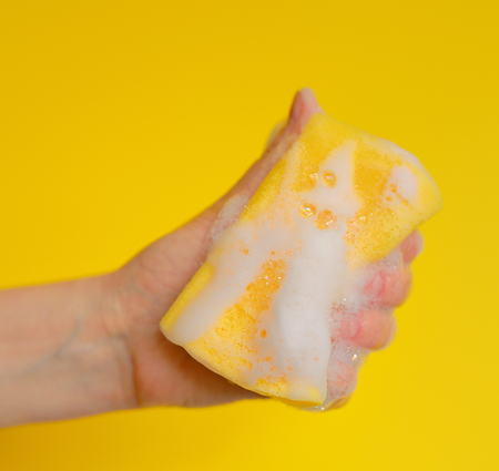 Hand with sponge with foam on yellow backgroundの写真素材