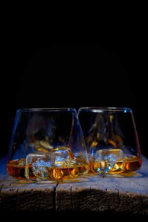 Glass of scotch whiskey and ice isolated on wooden tableの写真素材