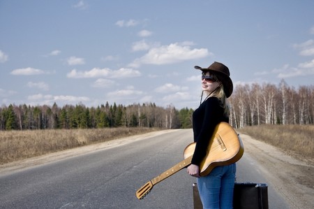 country girl with guitar goes on road solitary under skyの写真素材