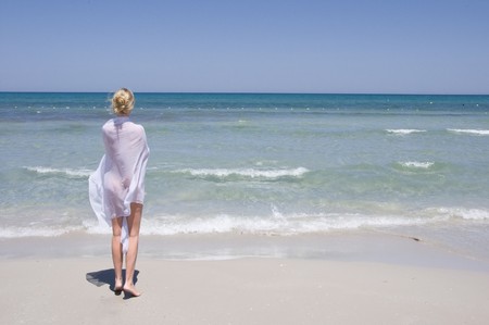beautiful young girl in white walking on the beach by the blue seaの写真素材