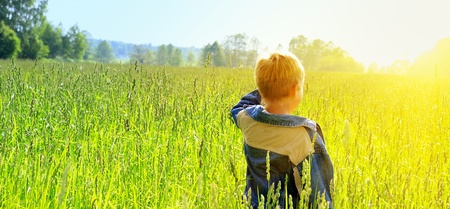happy young boy looking horizon and dreaming on green field grassの写真素材